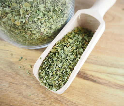 Messlöffel mit getrockneten Bio-Moringablättern auf einem Holztisch, ideal für Tee und Smoothies.