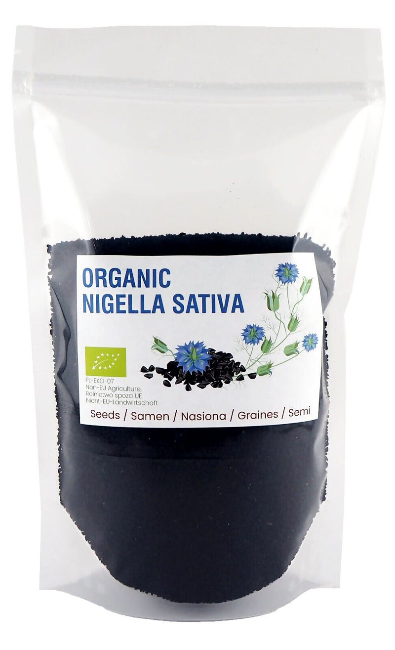 Das Foto zeigt eine Verpackung mit Nigellasamen, gekennzeichnet mit einem Etikett, das auf den ökologischen Ursprung hinweist, mit einer Illustration von blauen Blüten und einem Hinweis, dass die Samen biologisch sind, vor einem weißen Hintergrund.