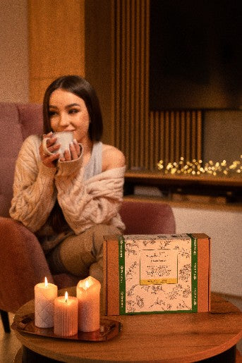Junge Frau genießt eine Tasse Winter Princess Tee zu Hause mit Kerzenlicht und Geschenkbox im Hintergrund.