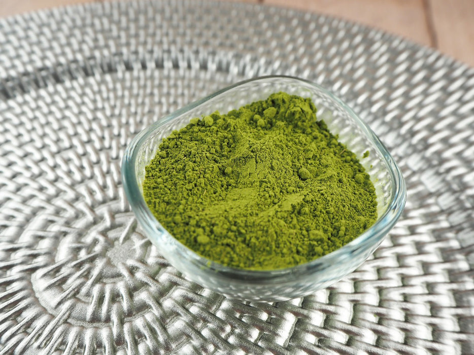 Klare Glasschale mit feinem, grünem Steviapulver auf einem dekorativen Untergrund, zuckerfreie Alternative für gesunde Ernährung.