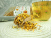 Getrocknete Ringelblumenblüten auf einem Holzlöffel mit Verpackung im Hintergrund, ideal für gesunde Tees und Naturheilkunde.