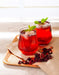 Zwei Gläser mit erfrischendem, rotem Hibiskustee und Eiswürfeln auf einem Holzbrett, garniert mit frischer Minz