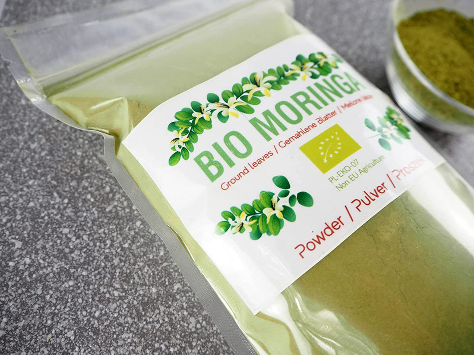 Detailansicht einer Packung Bio Moringa Pulver mit Produktinformationen auf dem Etikett, auf einer strukturierten Oberfläche.