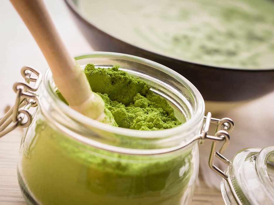 Grünes Bio Moringa Pulver in einem Glasgefäß mit Schließverschluss und einem Stößel auf einem hellen Küchentisch.