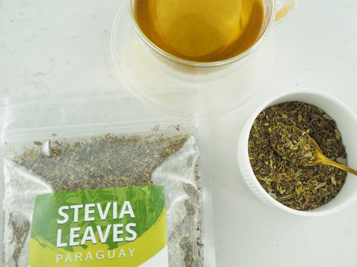 Transparente Packung mit getrockneten Steviablättern neben einer Tasse Tee, natürliche Süße ohne Kalorien.