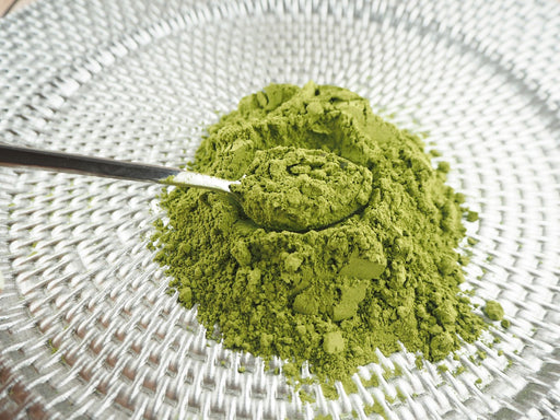 Ein Messlöffel voller grünen Steviapulvers auf einem gewebten Tischset, perfekt als natürlicher Süßstoff.