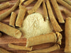 Ashwagandha-Pulver aufgestapelt zwischen mehreren getrockneten Ashwagandha-Wurzelstücken auf einem Holztisch.