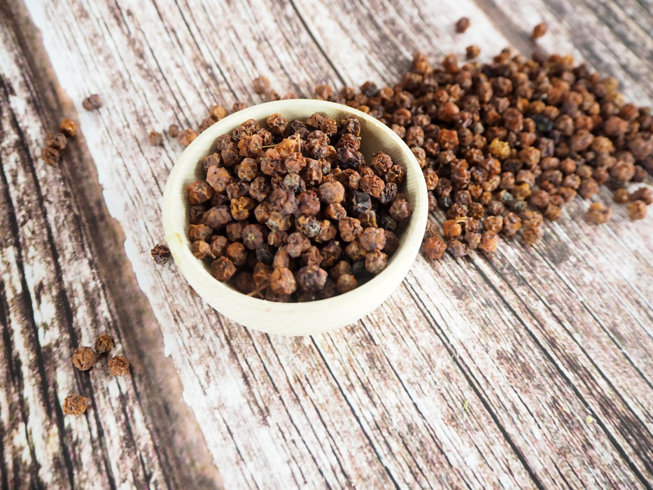 Kleine Schüssel mit getrockneten Vogelbeeren auf Holzuntergrund, ideal für traditionelle Rezepte.