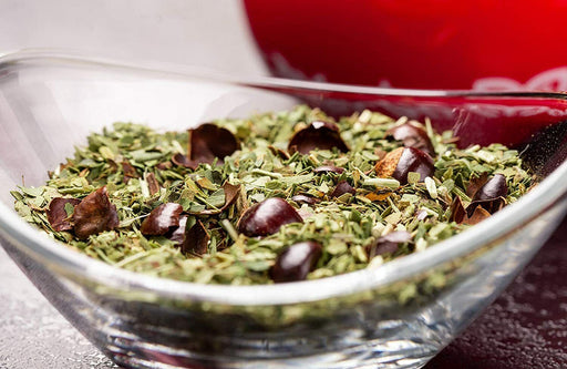 Traditionelle Mate-Tee-Zubereitung in einem roten Mate-Becher mit Metallstrohhalm, gefüllt mit grünen Mate-Blättern.